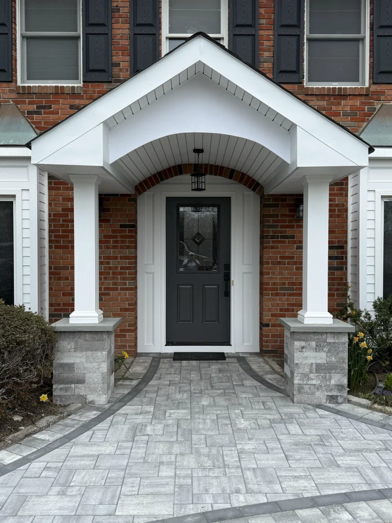 A formal front entrance walkway featuring light grey pavers with a dark charcoal border leading to a white portico.