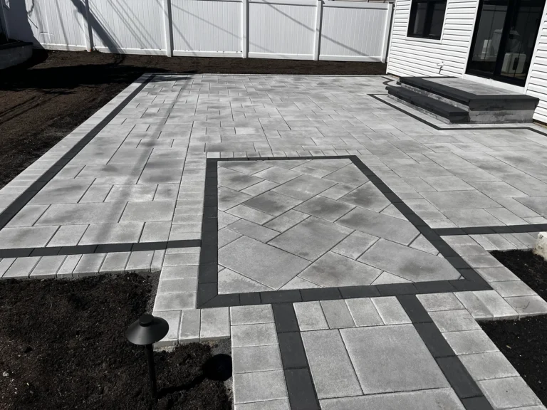 A large backyard patio using oversized grey stone pavers with dark charcoal accent lines.