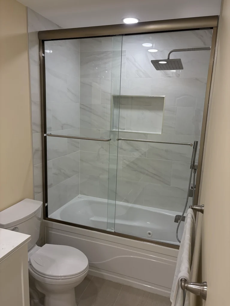 Clean white bathroom featuring large format wall tiles and a bronze-framed sliding glass shower door.