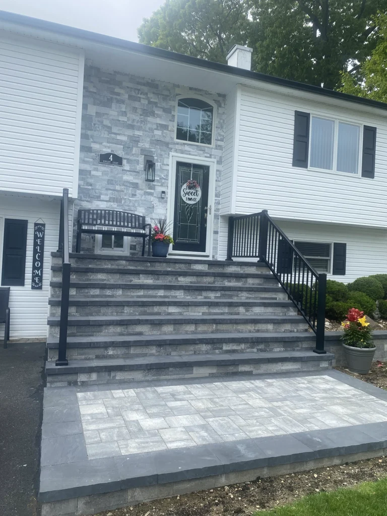 Wide multi-level stone steps with black metal railings leading to a light stone veneer front door.